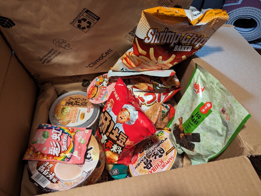 Shipping box open and showing an assortment of instant ramen and snacks.